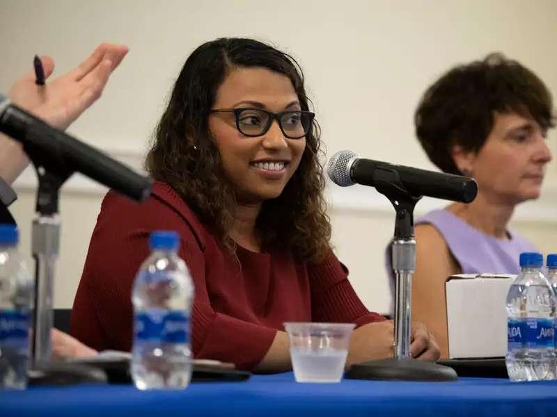 two women seated at a table, speaking on a panel